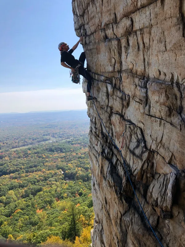 Rock climber ascending a steep cliff face with autumn landscape in the background