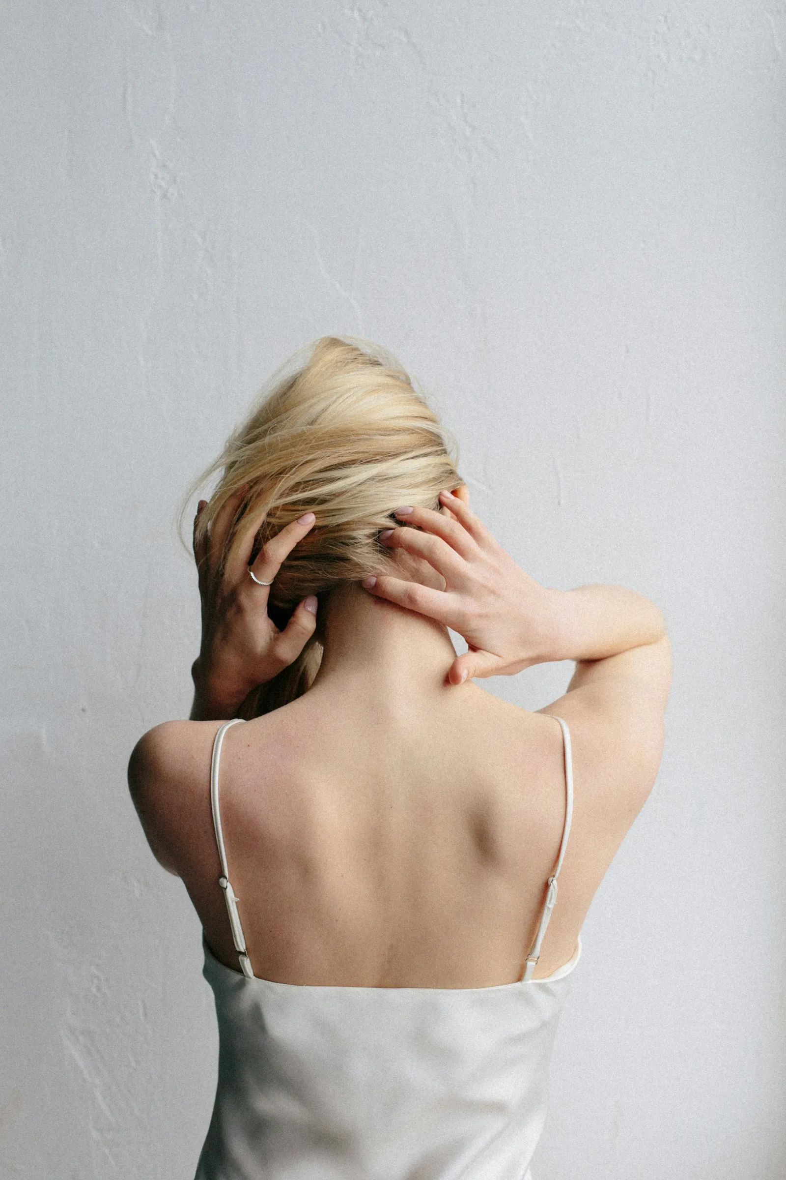 A woman seen from behind, lifting her hair away from her neck and upper back