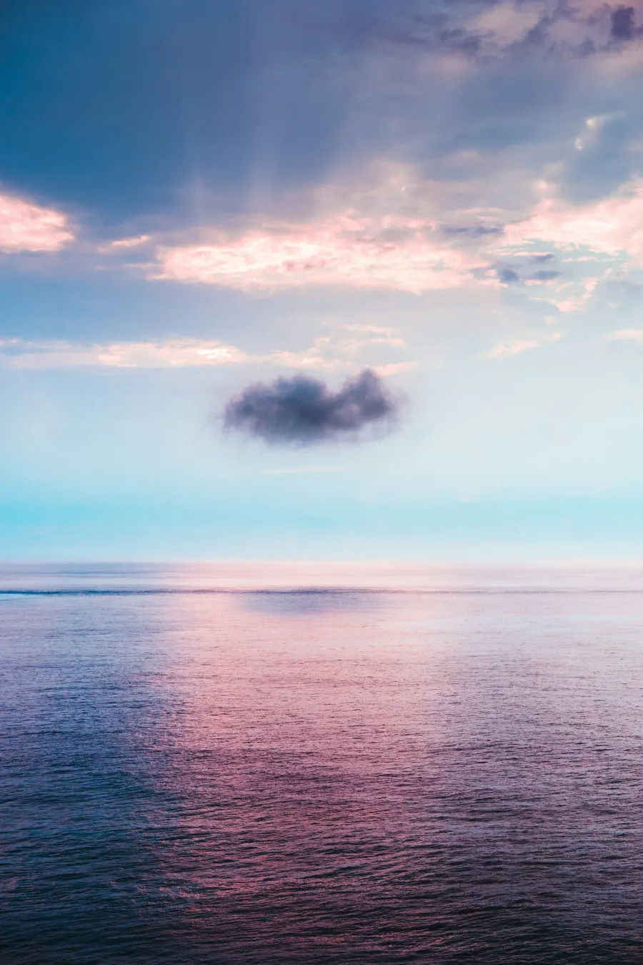 Ocean at sunset with a single cloud and pink reflections on the water.