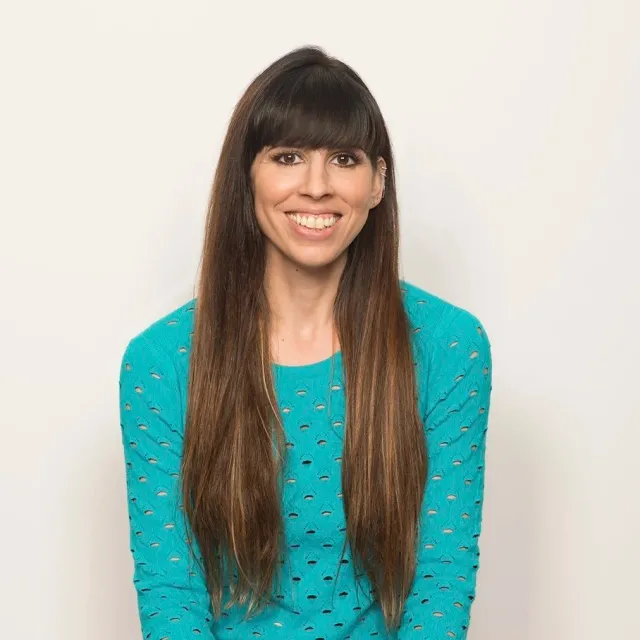 Smiling woman with long brown hair wearing a turquoise sweater against a neutral background