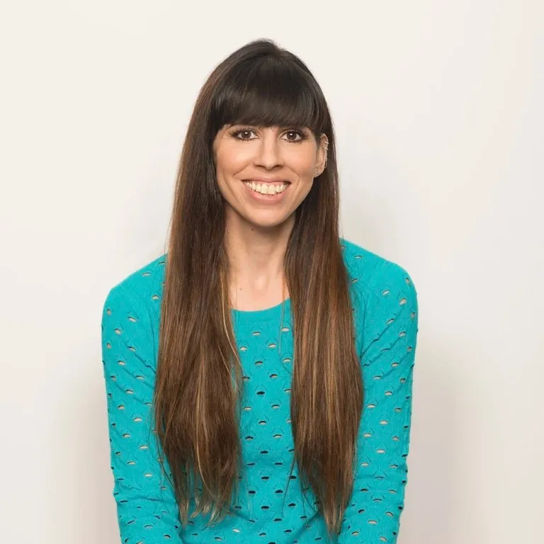 Smiling woman with long brown hair wearing a turquoise sweater against a neutral background