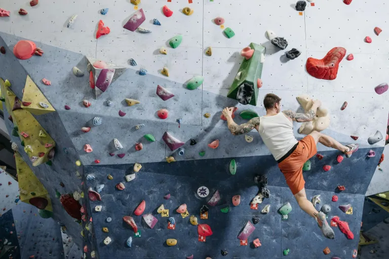 Person wearing orange shorts and white tank top climbing an indoor rock climbing wall with colorful holds