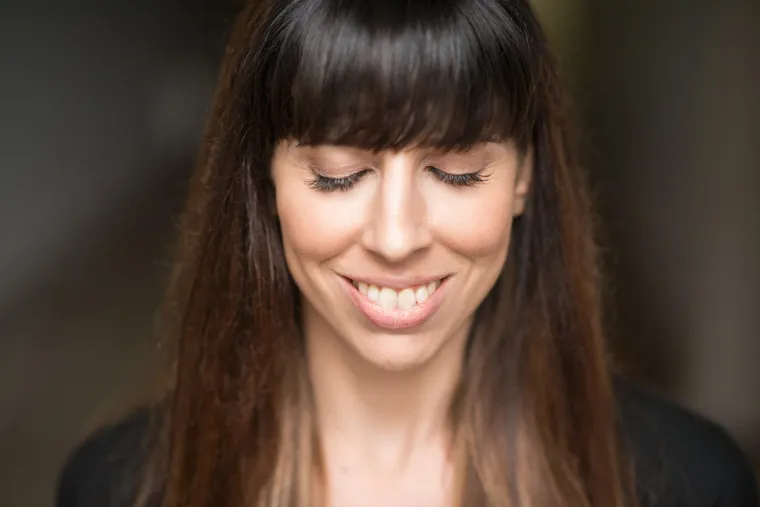 Woman with long hair and bangs smiling with eyes closed.