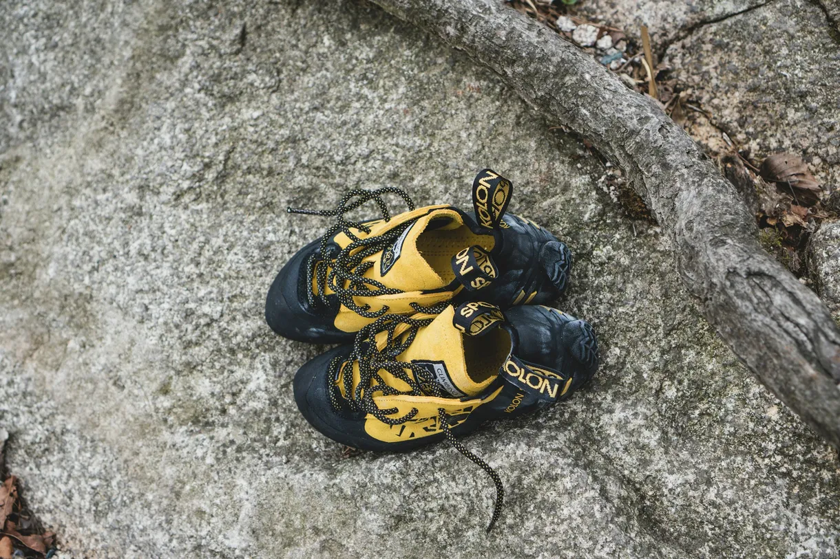 A worn pair of yellow and black lace-up climbing shoes lying on granite