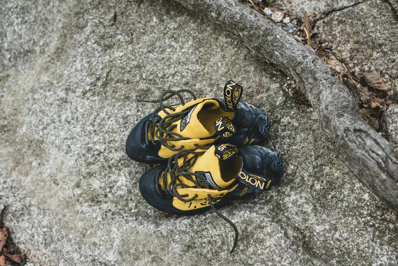 A worn pair of yellow and black lace-up climbing shoes lying on granite