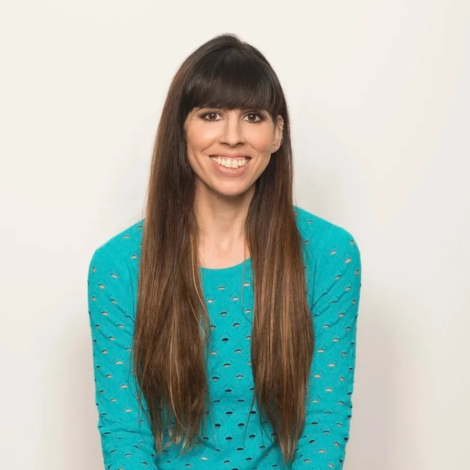 Smiling woman with long hair wearing a teal sweater against a white background.